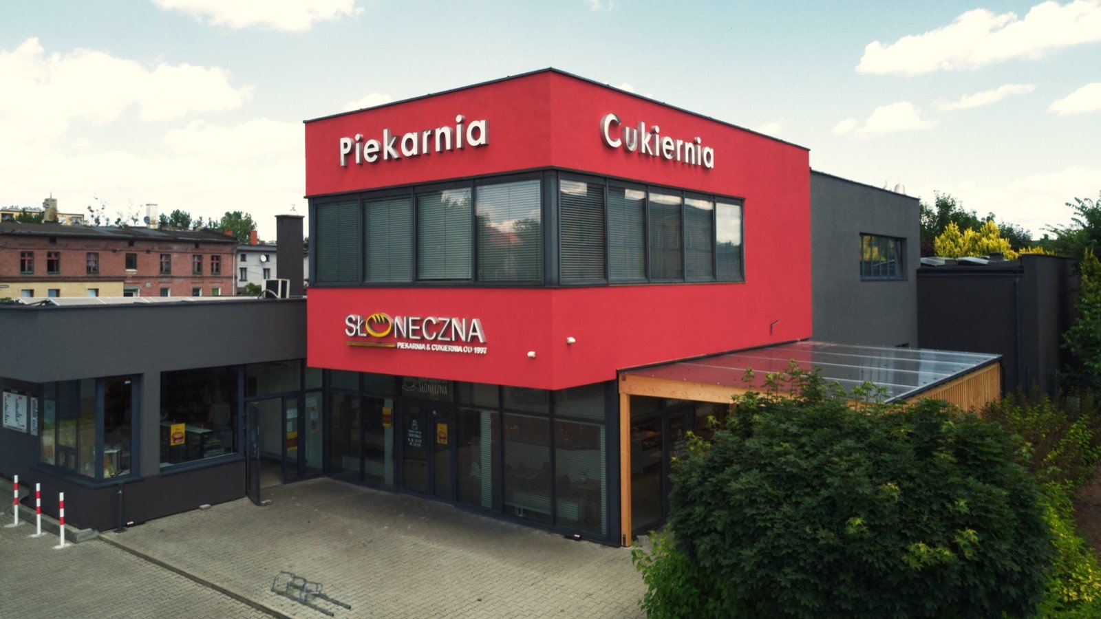Budynek piekarni Cukierni Słonecznej — czerwona elewacja z szyldem „Piekarnia Cukiernia” i witryną sklepową